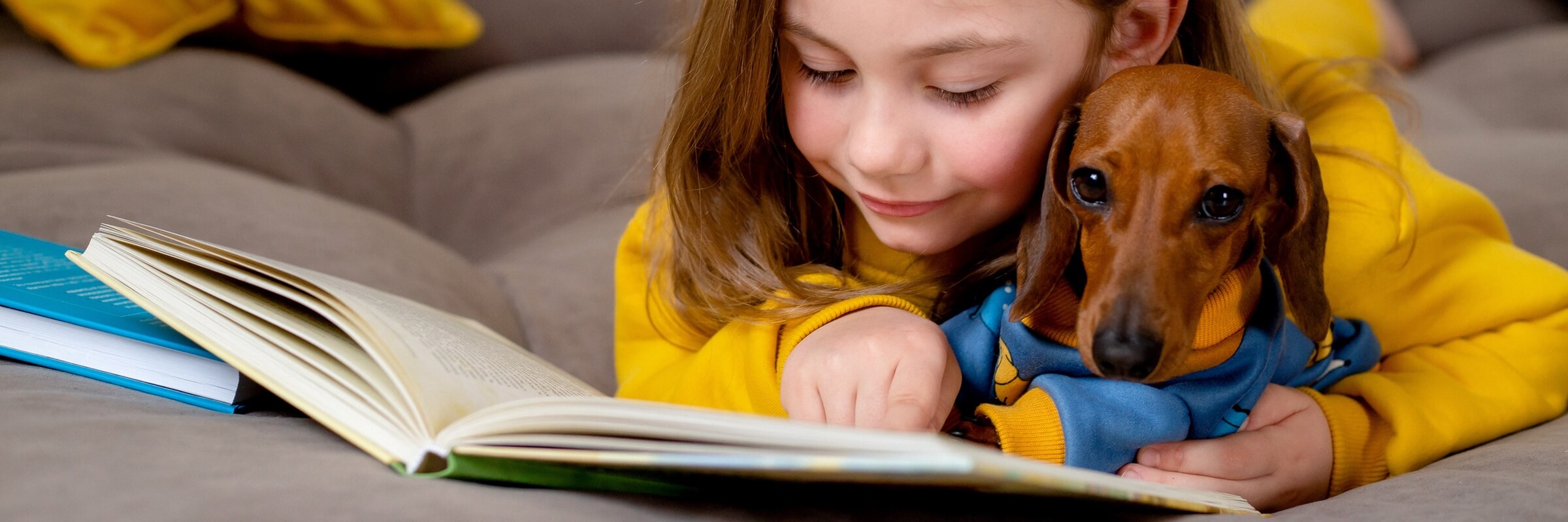 Young girl lying on bed with dachshund appearing to read a book together